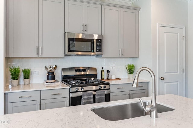 kitchen with stainless steel appliances, decorative backsplash, a sink, and gray cabinetry