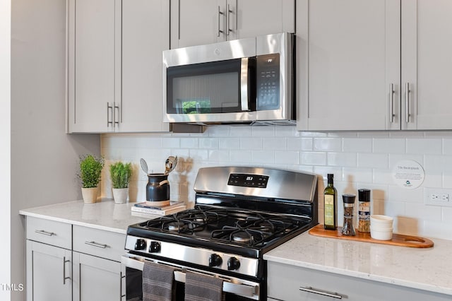 kitchen featuring appliances with stainless steel finishes, gray cabinets, backsplash, and light stone countertops