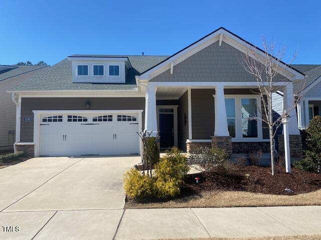 craftsman house featuring covered porch, concrete driveway, stone siding, and an attached garage