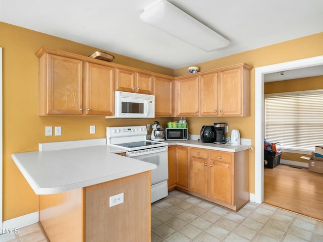 kitchen featuring light brown cabinets, a peninsula, white appliances, and light countertops