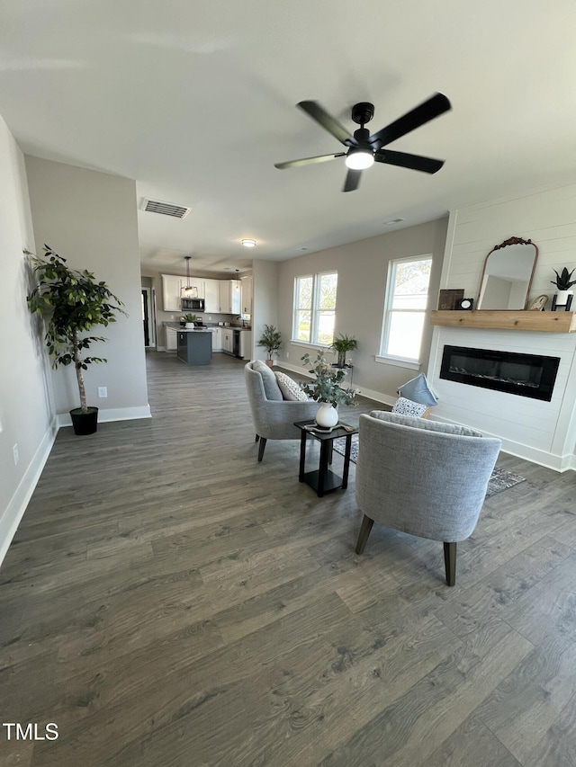 living room featuring a glass covered fireplace, dark wood-style flooring, visible vents, and baseboards