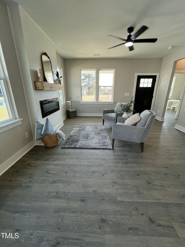 living area featuring dark wood-style floors, a glass covered fireplace, arched walkways, and baseboards