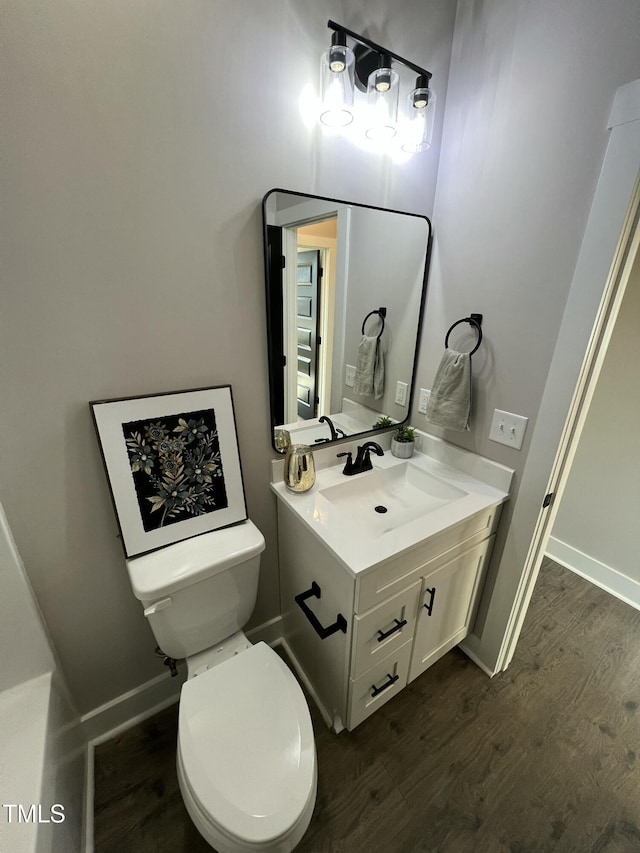 bathroom with toilet, wood finished floors, vanity, and baseboards