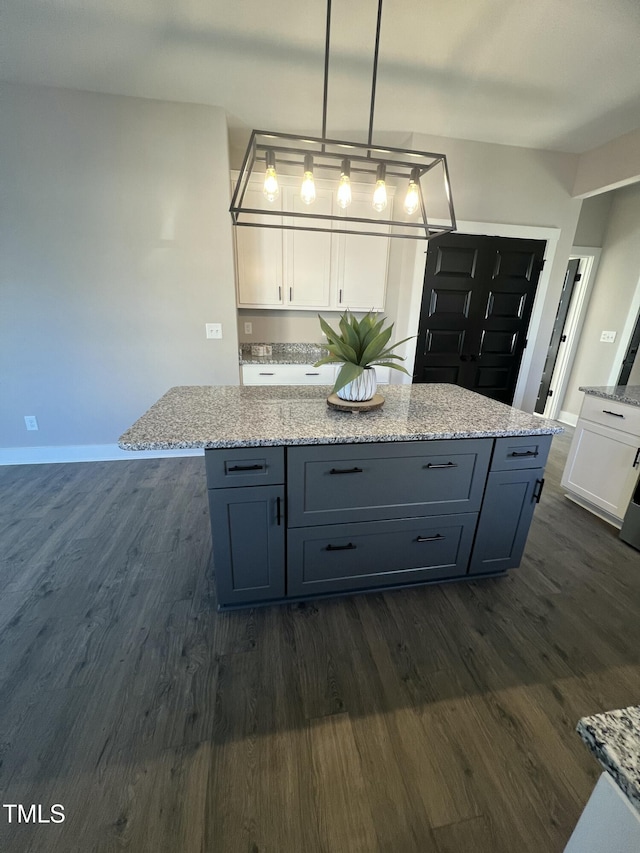 kitchen with light stone countertops, white cabinets, dark wood-type flooring, and a center island