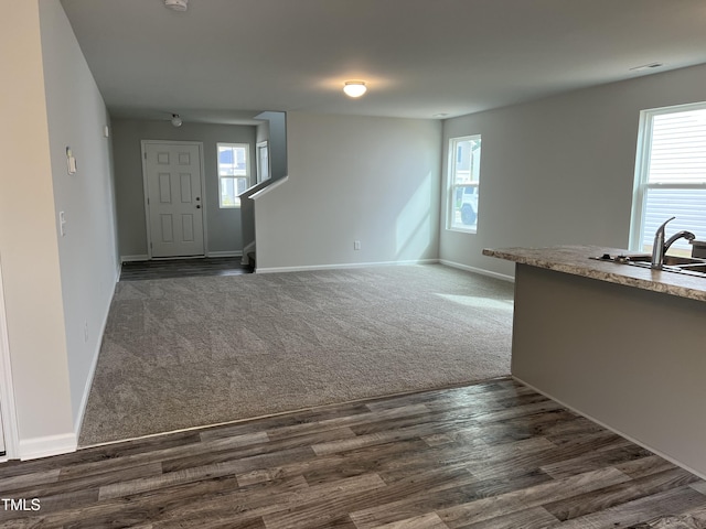 unfurnished living room with dark carpet, baseboards, a wealth of natural light, and a sink