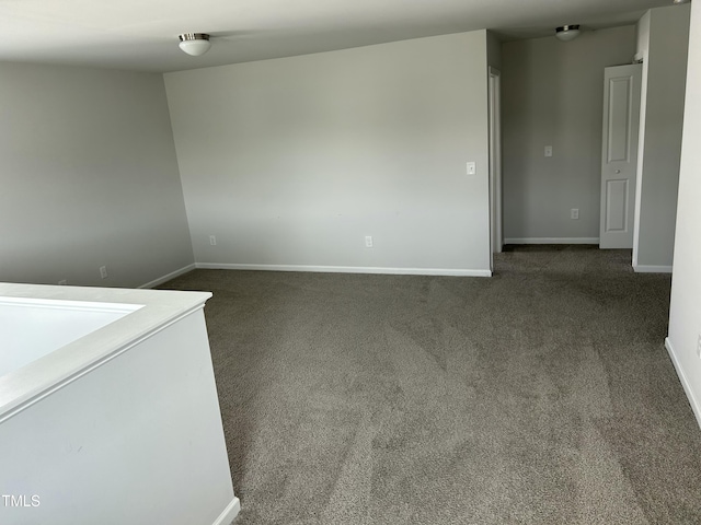 unfurnished room featuring baseboards and dark carpet