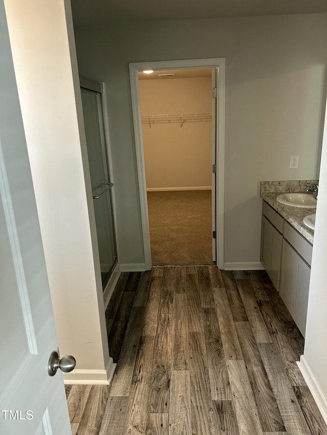 full bath featuring a walk in closet, wood finished floors, a shower stall, baseboards, and vanity