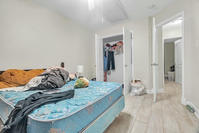 bedroom featuring light wood finished floors, a closet, a spacious closet, attic access, and baseboards