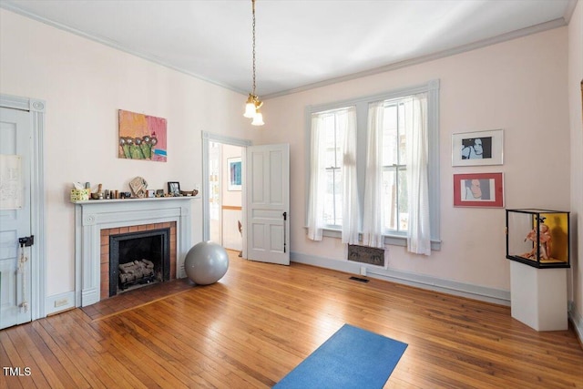 workout area featuring crown molding, visible vents, a tiled fireplace, and hardwood / wood-style floors