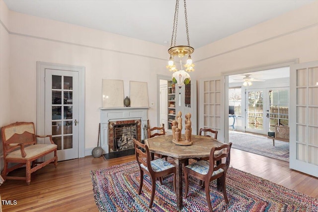 dining room with a fireplace with raised hearth, wood finished floors, and french doors