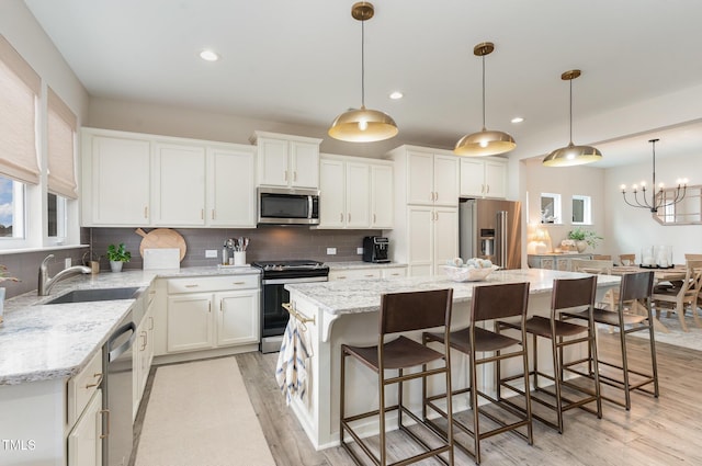 kitchen with light wood-style flooring, stainless steel appliances, a sink, white cabinets, and decorative backsplash