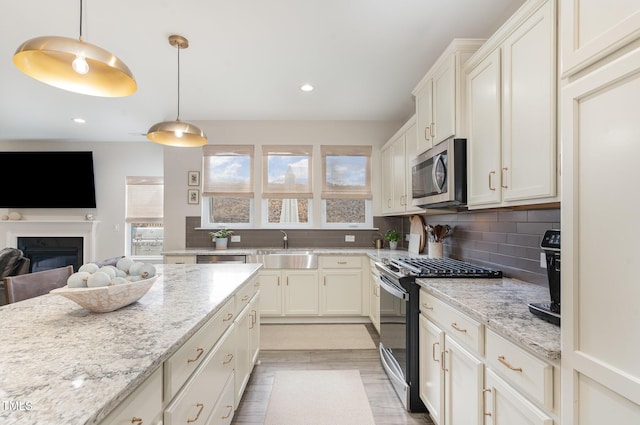 kitchen featuring decorative backsplash, stainless steel microwave, light stone countertops, a sink, and gas stove