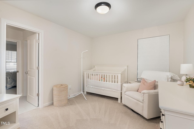 bedroom with baseboards, a nursery area, and light colored carpet