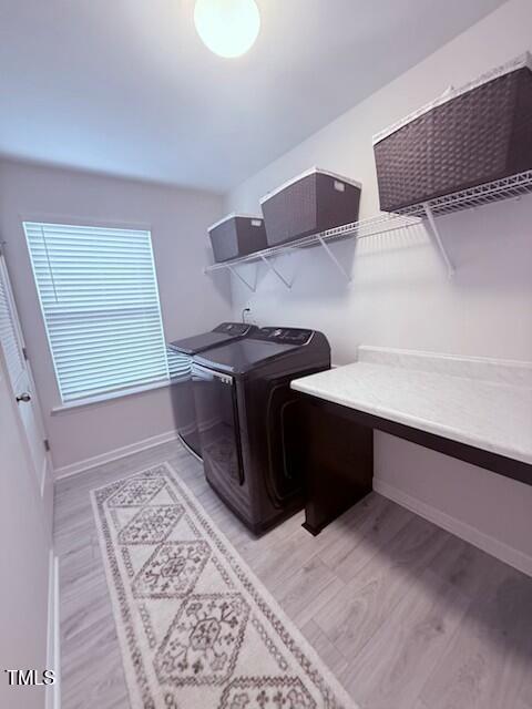 clothes washing area featuring light wood-type flooring, laundry area, washing machine and dryer, and baseboards