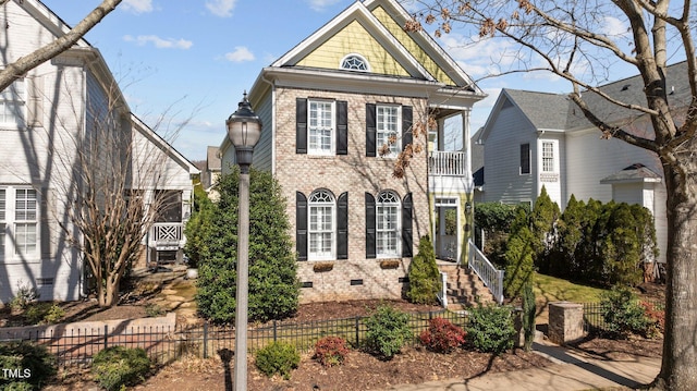 view of front of house with crawl space, brick siding, a fenced front yard, and a balcony