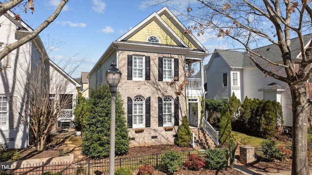 view of front of property featuring a balcony, brick siding, a fenced front yard, and crawl space