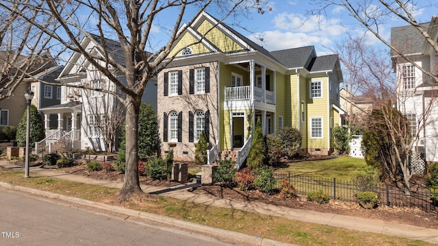 view of front of home featuring a fenced front yard, a shingled roof, crawl space, a balcony, and brick siding