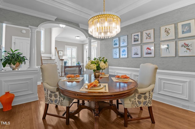 dining space with ornamental molding, wood finished floors, arched walkways, wainscoting, and ornate columns