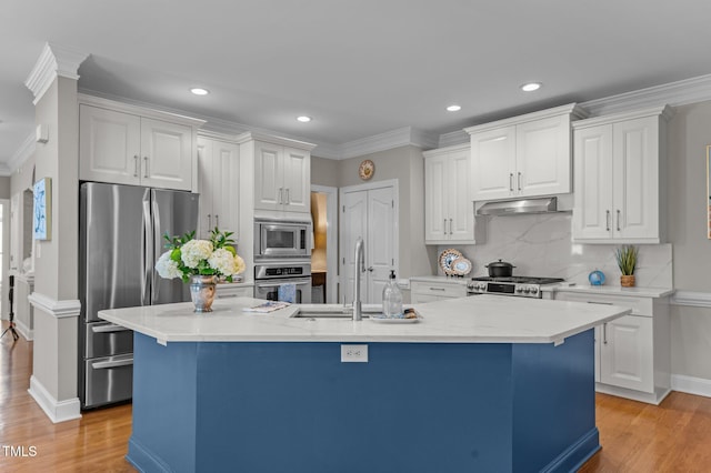 kitchen featuring an island with sink, a sink, stainless steel appliances, under cabinet range hood, and crown molding