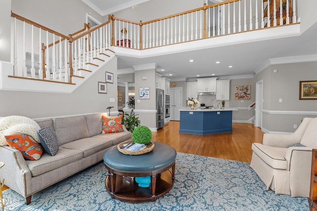 living area with stairway, crown molding, light wood-style floors, and a towering ceiling