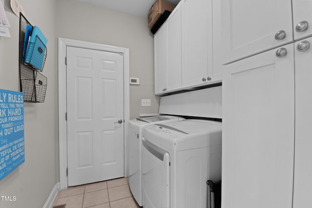 laundry area featuring washing machine and clothes dryer, light tile patterned floors, cabinet space, and baseboards