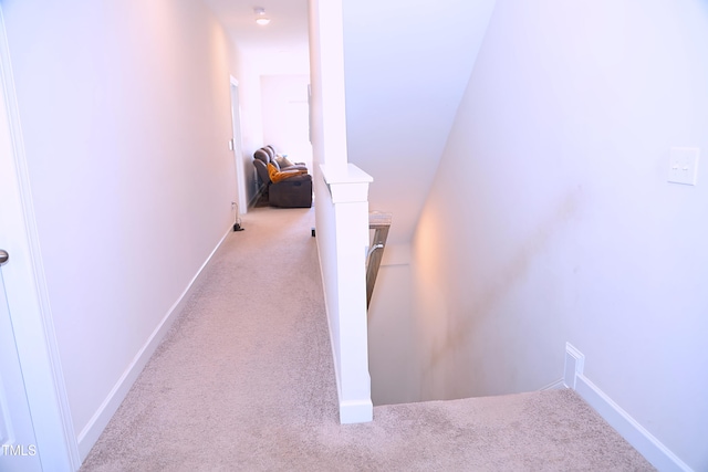 hallway featuring carpet floors, baseboards, and an upstairs landing