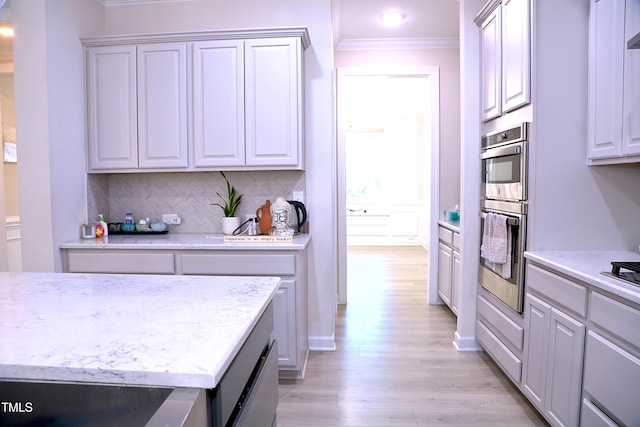 kitchen with stainless steel double oven, ornamental molding, decorative backsplash, light stone countertops, and light wood finished floors