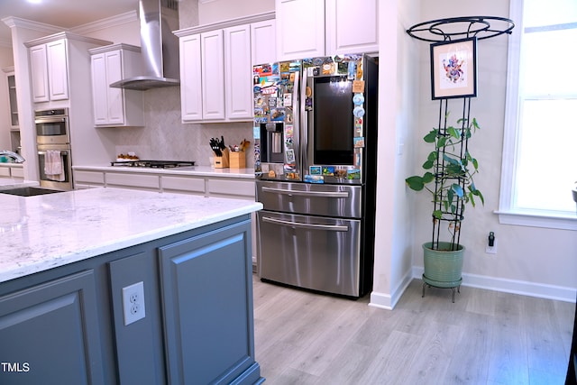 kitchen with stainless steel appliances, light wood-style flooring, white cabinetry, a sink, and wall chimney range hood