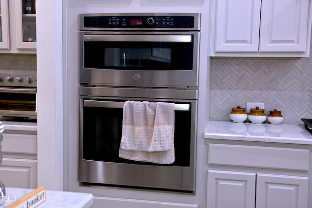 kitchen with double oven, light stone counters, white cabinets, and backsplash