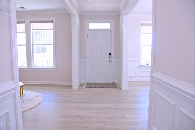 entrance foyer with visible vents, a wainscoted wall, ornamental molding, light wood-type flooring, and a decorative wall