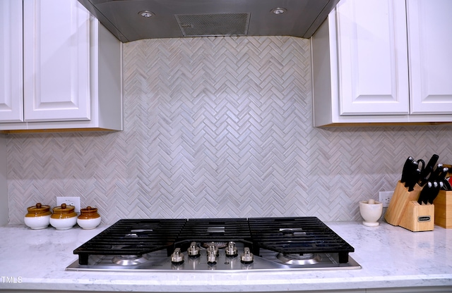 kitchen with light stone counters, exhaust hood, white cabinets, decorative backsplash, and stainless steel gas stovetop