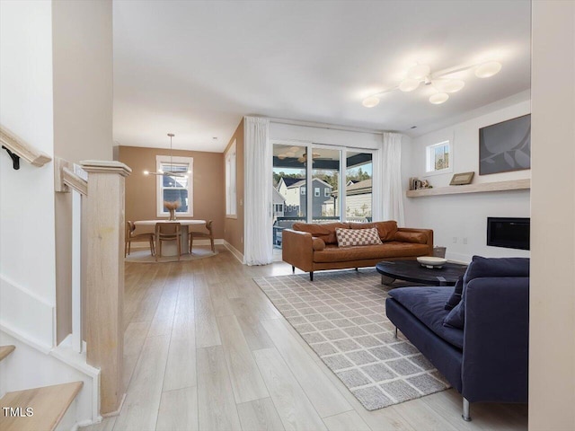 living room featuring stairs, light wood-type flooring, a fireplace, and a wealth of natural light
