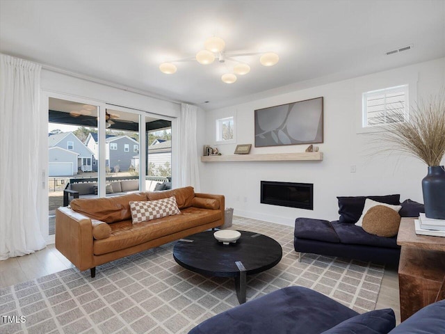 living room featuring wood finished floors, a glass covered fireplace, and visible vents