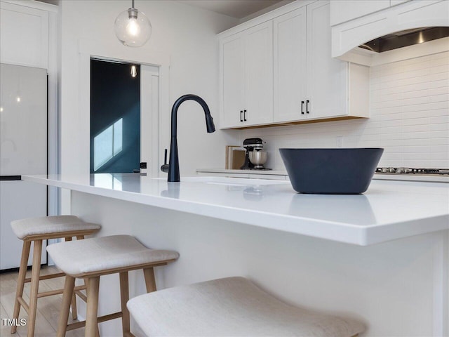kitchen with white cabinetry, a kitchen breakfast bar, custom exhaust hood, freestanding refrigerator, and decorative backsplash
