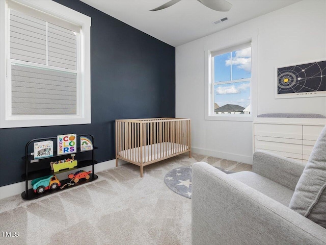 bedroom featuring ceiling fan, visible vents, baseboards, a crib, and carpet