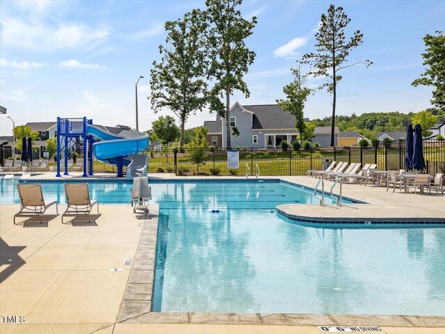 community pool with fence, a water slide, and a patio