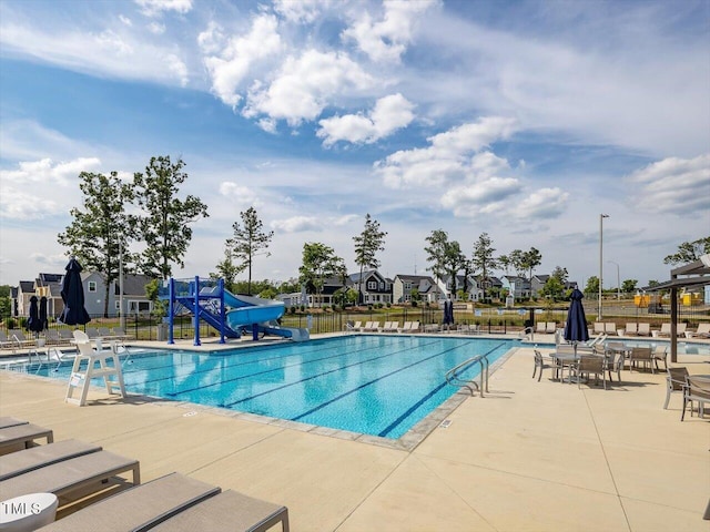 pool with a residential view, fence, a water slide, and a patio
