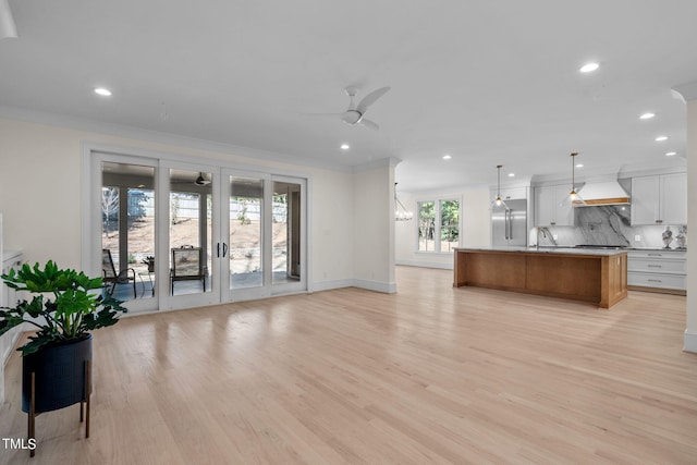 kitchen with a sink, light wood-style floors, open floor plan, custom exhaust hood, and tasteful backsplash