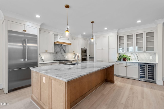 kitchen featuring light wood-style flooring, wine cooler, built in appliances, premium range hood, and a sink