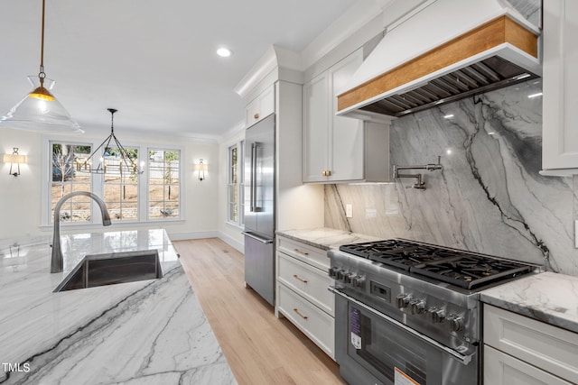 kitchen with high end appliances, hanging light fixtures, white cabinetry, a sink, and premium range hood