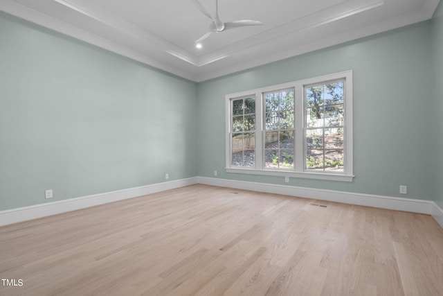 empty room featuring a ceiling fan, visible vents, baseboards, light wood-type flooring, and a tray ceiling