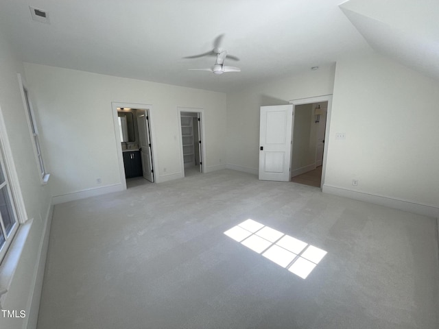 unfurnished bedroom with visible vents, light colored carpet, ensuite bathroom, a spacious closet, and vaulted ceiling