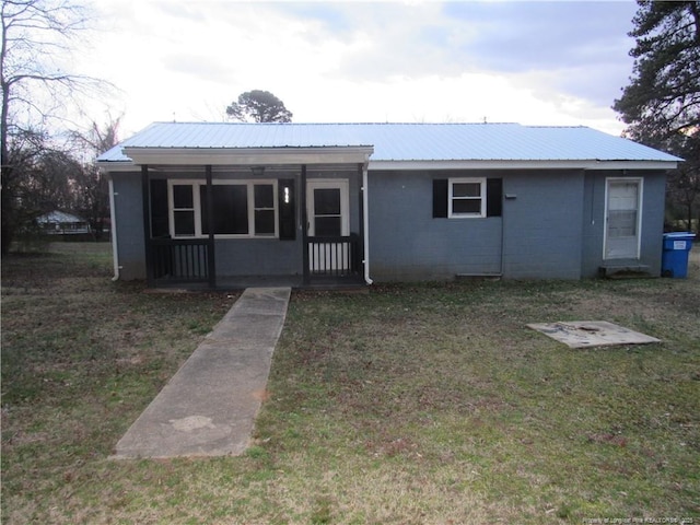 view of front facade with concrete block siding, covered porch, metal roof, and a front lawn