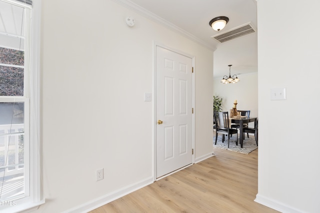 hall with a chandelier, light wood-style flooring, visible vents, baseboards, and crown molding