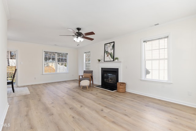 unfurnished living room featuring light wood-style floors, ornamental molding, a wealth of natural light, and a glass covered fireplace