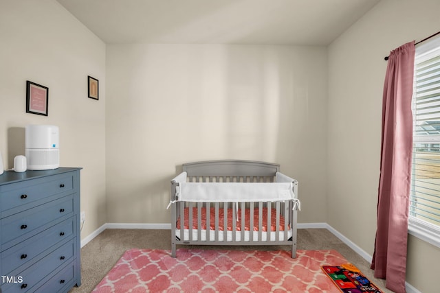 carpeted bedroom featuring a crib and baseboards