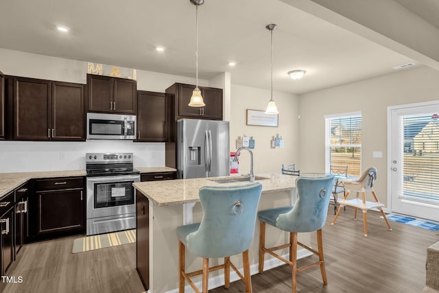 kitchen with light wood finished floors, a breakfast bar area, appliances with stainless steel finishes, decorative light fixtures, and a sink