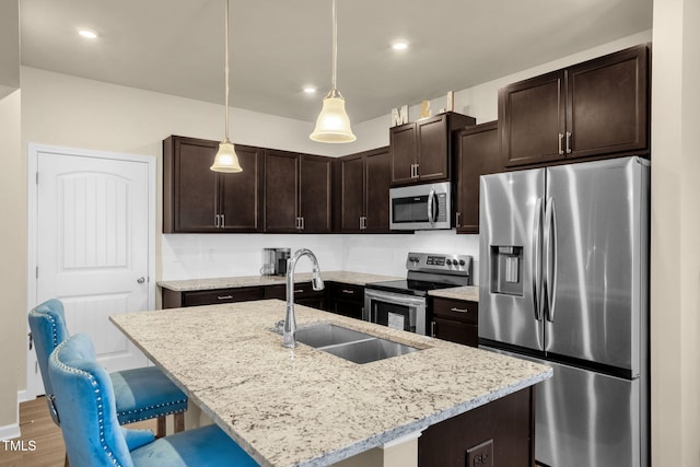 kitchen with light stone counters, appliances with stainless steel finishes, dark brown cabinets, a kitchen bar, and a sink