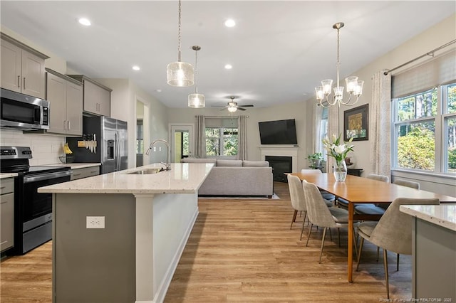 kitchen with gray cabinetry, stainless steel appliances, a sink, light wood-style floors, and decorative backsplash