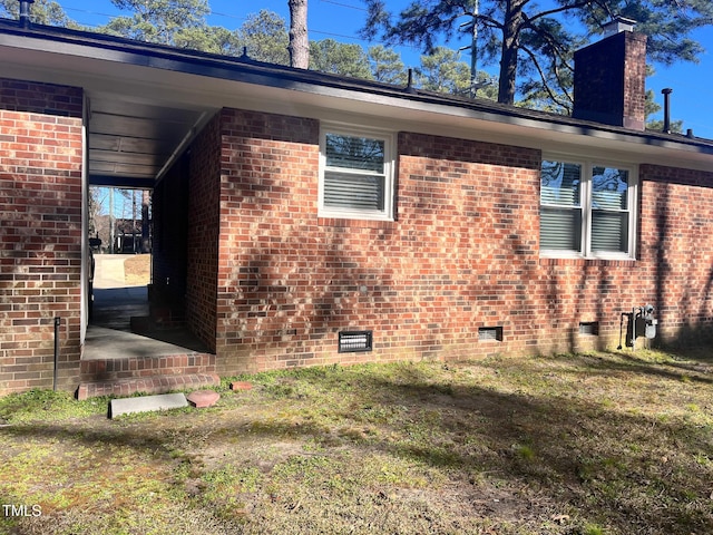 view of side of property with crawl space, brick siding, a yard, and a chimney